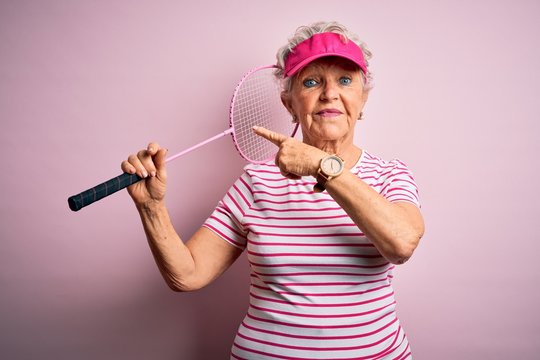 Senior beautiful sportswoman holding badminton racket over isolated pink background very happy pointing with hand and finger