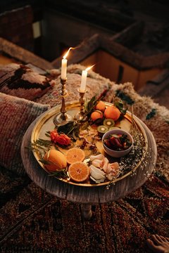 From above composition of assorted fresh fruits and plants served on golden tray with burning candles on round wooden table in Moroccan style