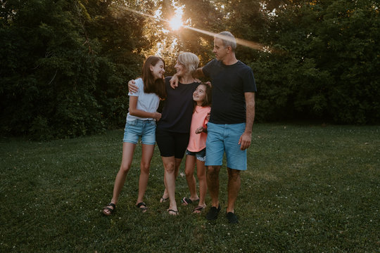 Happy adult couple with adorable daughters standing on grass near green trees and smiling while resting together and enjoying summer day in nature