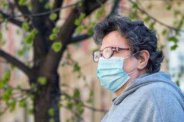 Portrait of an elderly adult woman in a protective medical mask. Senior mature female senior citizen is sad outside. Retirement epidemic and pandemic concept.