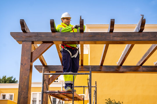 From below side view of male technician in work wear standing on scaffolding and preparing for installation of solar panel on wooden construction