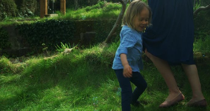 Little preschooler chasing bubbles around his mother on the lawn