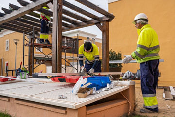 Group of male technicians in uniform working with alternative solar panels and preparing for installation near residential building