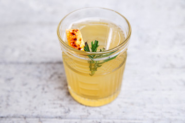 Fresh penicillin alcoholic cocktail with a slice of orange and ice cubes. An alcoholic Scottish penicillin cocktail with lemon, ginger sprig of rosemary and burnt sugar. light white gray background