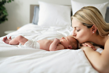A woman with a newborn baby in bed kiss her