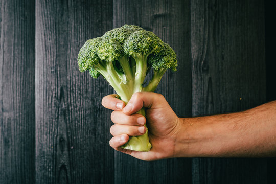 Unrecognizable person grasping and showing healthy fresh broccoli against black lumber wall while being on diet
