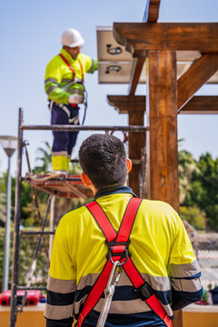 Group of workers in uniform and helmets installing photovoltaic panels on roof of wooden construction near house