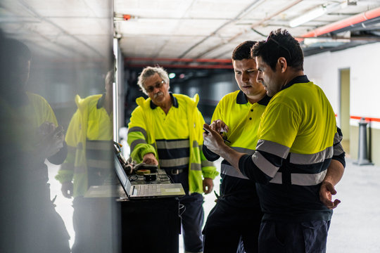 Group of skilled male engineers in uniform using gadgets while examining electrical equipment in modern building