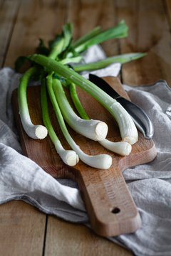 Bunch of ripe scallions placed on wooden cutting board and cloth napkin on rustic table in kitchen