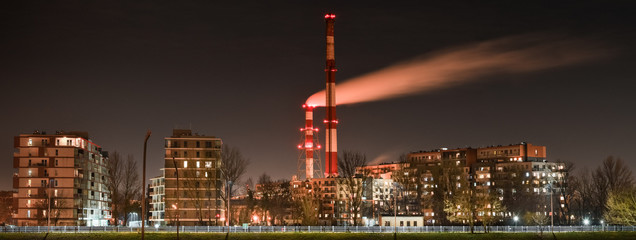 Fototapeta premium Night view of the smoke coming out of the chimney over apartment blocks in the city.