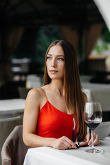 Beautiful young girl sits and drinks wine on the veranda of a beautiful house. Holiday.