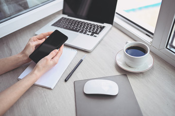 Female hands using smart phone in interior workplace, freelance business woman using cell phone at office desk, working from home using smart phone and notebook computer. Remote worker quarantine