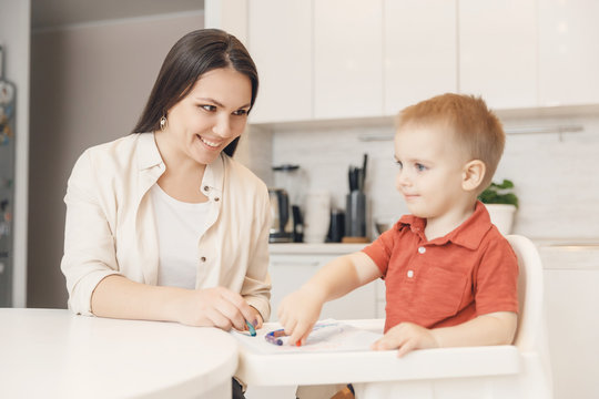 Mom teaches her son to draw with pencils on paper white kitchen background