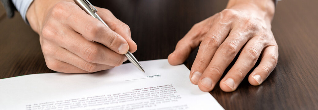 A businessman sits at an office Desk and signs a contract with a ballpoint pen - Powered by Adobe