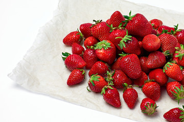 Heap of fresh ripe strawberries on white crumpled paper over white background. Selective focus