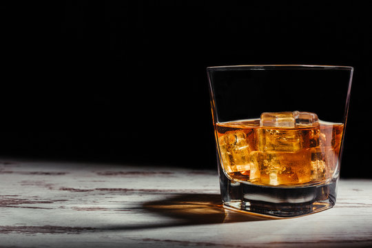 Glass of scotch in rays on aged rustic table in darkness