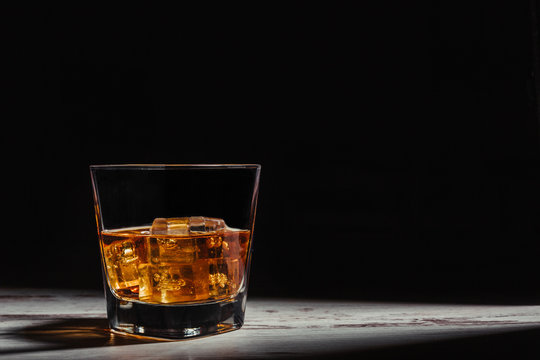 Glass of scotch in rays on aged rustic table in darkness
