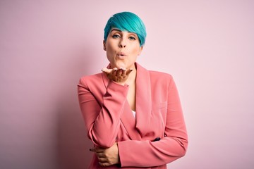Young beautiful businesswoman with blue fashion hair wearing jacket over pink background looking at...
