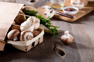 Delivery of products. Champignon mushrooms and fresh greens in eco-friendly packaging on a wooden...