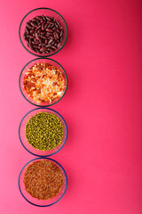 Glass jars with cereal mung bean, lentils, beans, brown rice on a pink background.