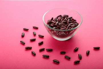 Glass jar with red beans on a pink background.