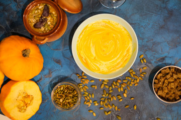 Roasted pumpkin and carrot soup with cream and pumpkin seeds on white wooden background. Copy space