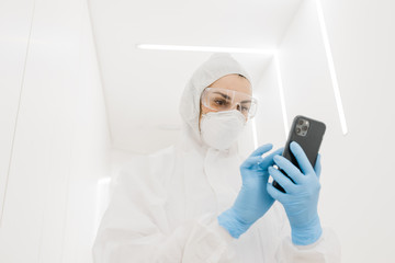 A girl doctor in a protective suit during an epidemic covid communicates on the phone in the white corridor of the hospital.