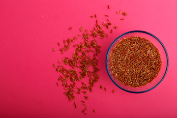 Glass jar with brown rice on a pink background.