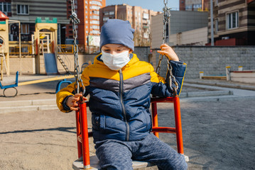 A small boy in a mask walks on the Playground during the quarantine. Stay at home