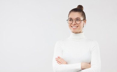 Horizontal banner of young business girl wearing glasses, standing with arms crossed and looking aside with smile, isolated on gray background with copy space