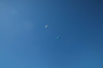 Two skydivers parachuting in the bright blue sky, looking up from below