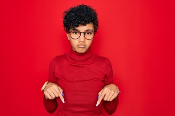 Fototapeta na wymiar Young beautiful african american afro woman wearing turtleneck sweater and glasses Pointing down looking sad and upset, indicating direction with fingers, unhappy and depressed.