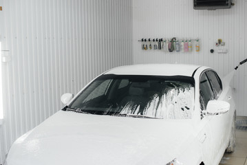 Modern washing with foam and high-pressure water of a white car. Car wash