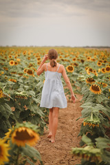 Pretty teen girl walking away through a field of sunflowers