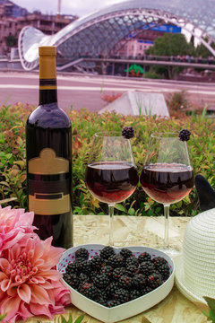 Still life on the nature of grapes, wine, hats and flowers on the background of the glass bridge of the world in Tbilisi, Georgia.