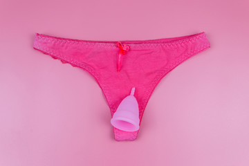 Women's panties with menstrual cup on pastel pink background. Top view. Concept of critical days,...