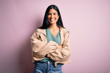 Young beautiful hispanic fashion woman wearing winter jacket and sweater over pink background happy face smiling with crossed arms looking at the camera. Positive person.