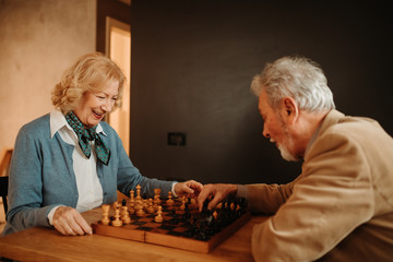 Portrait of senior couple playing chess at living room.