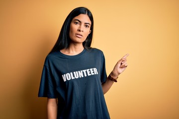 Young beautiful hispanic woman wearing volunteer t-shirt as social charity moral Pointing with hand...
