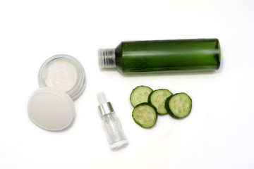 Cosmetic bottles and opened jar of facial or body cream and fresh cucumber.