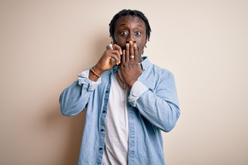 African american man having conversation talking on the smartphone over white background cover mouth with hand shocked with shame for mistake, expression of fear, scared in silence, secret concept