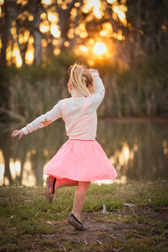 Little girl dancing by the river at sunset