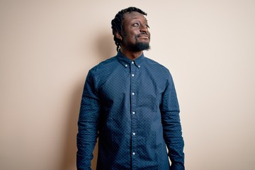 Young handsome african american man wearing casual shirt standing over white background smiling looking to the side and staring away thinking.