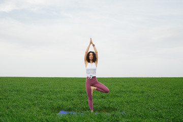 Young slim girl doing yoga outdoors in a green field