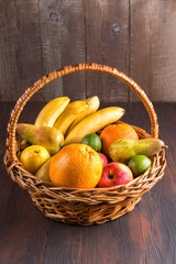 Fresh fruits in a basket on wooden table.