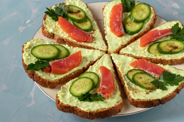 Six sandwiches with avocado paste, cucumbers and salted salmon on plate on light blue background, Closeup, Top view