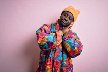 Young handsome african american man wearing colorful coat and cap over pink background sleeping...