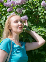woman in spring next to a bush of blossoming lilacs..