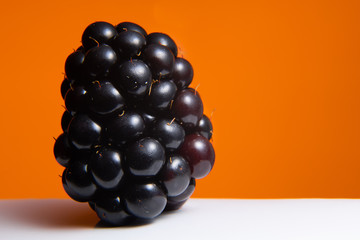 A solitary blackberry set against a bright orange background