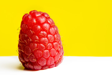 A solitary raspberry set against a bright yellow background
